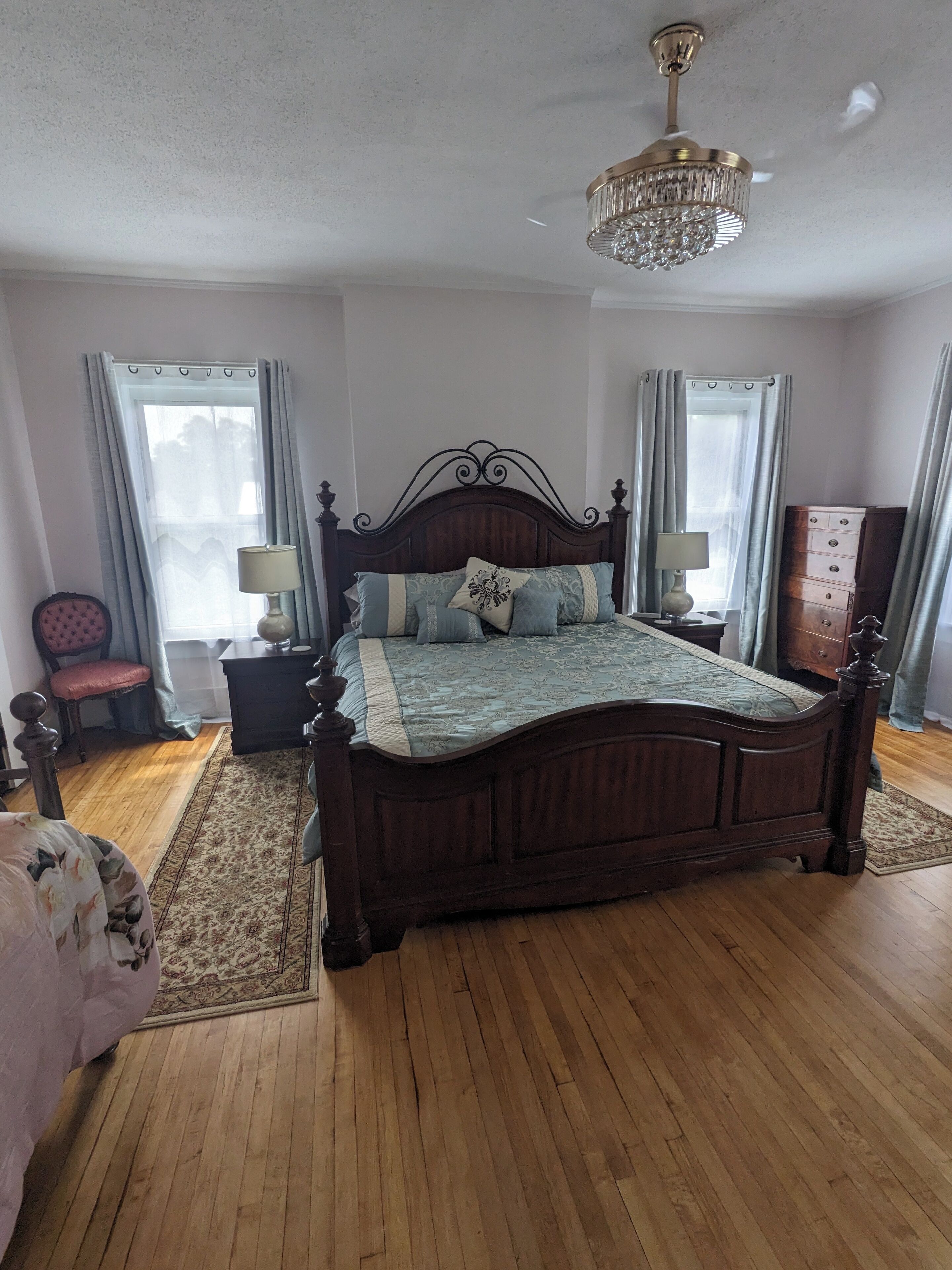 A bedroom with a wooden bed, two bedside tables with lamps, a chandelier, and a dresser.