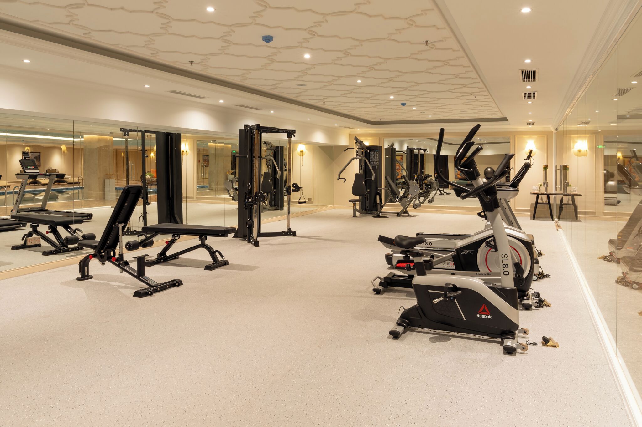 A spacious gym with various exercise equipment, including treadmills and weight machines, and a large mirror wall.