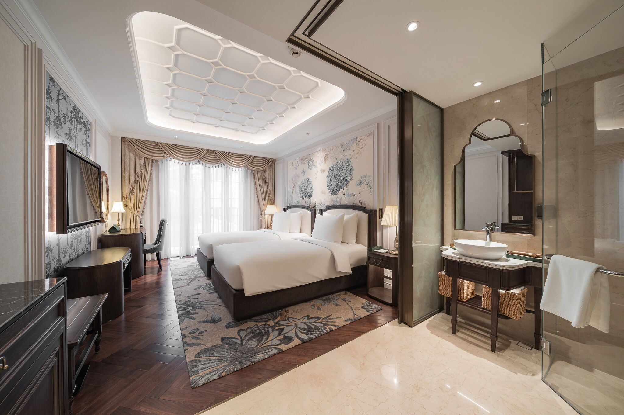 A modern hotel room with a large bed, a glass-enclosed shower, a vanity with a mirror, and a decorative ceiling light.