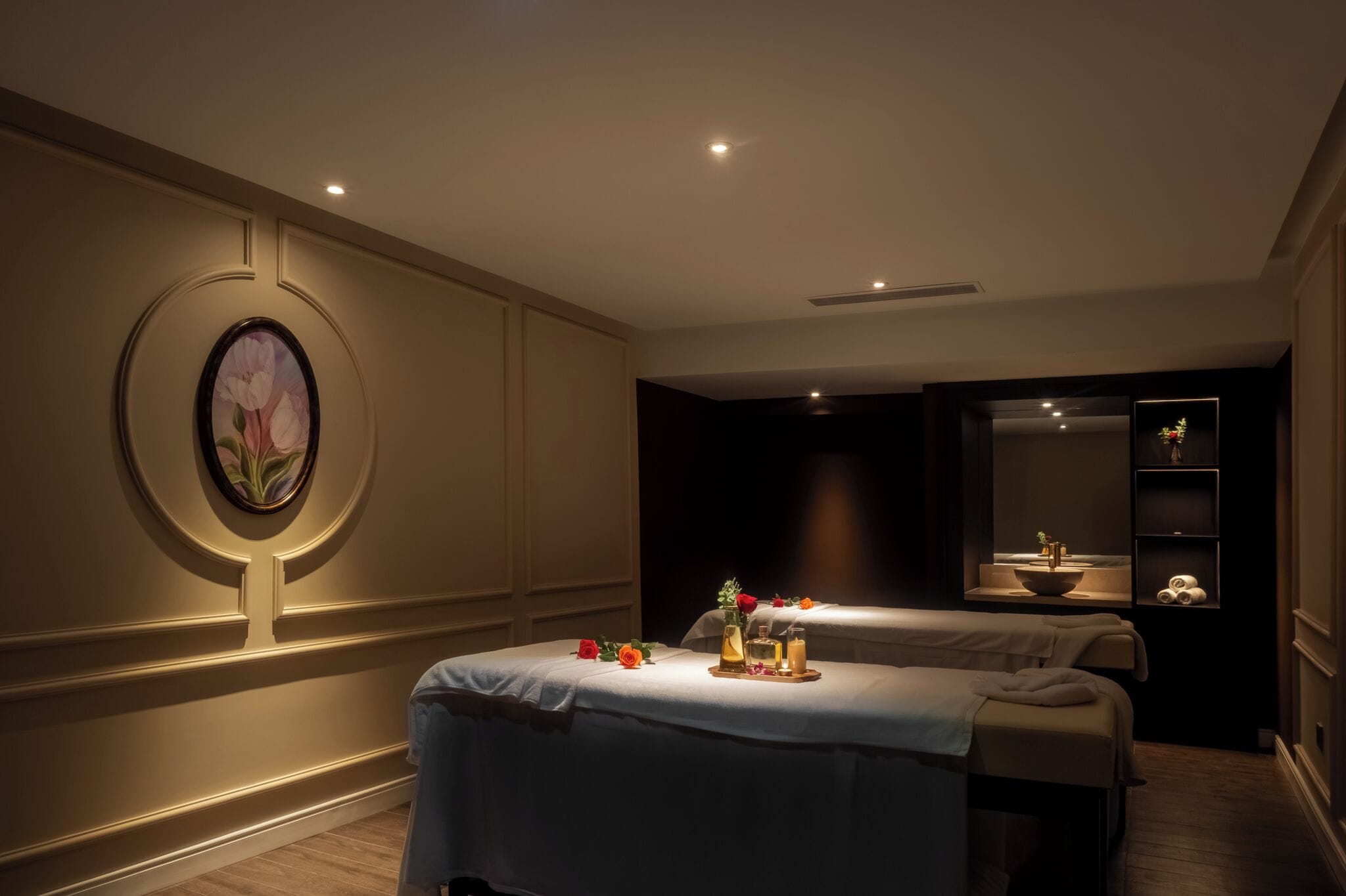 A spa room with two massage tables, a wall-mounted painting, and a small shelf with decorative items.