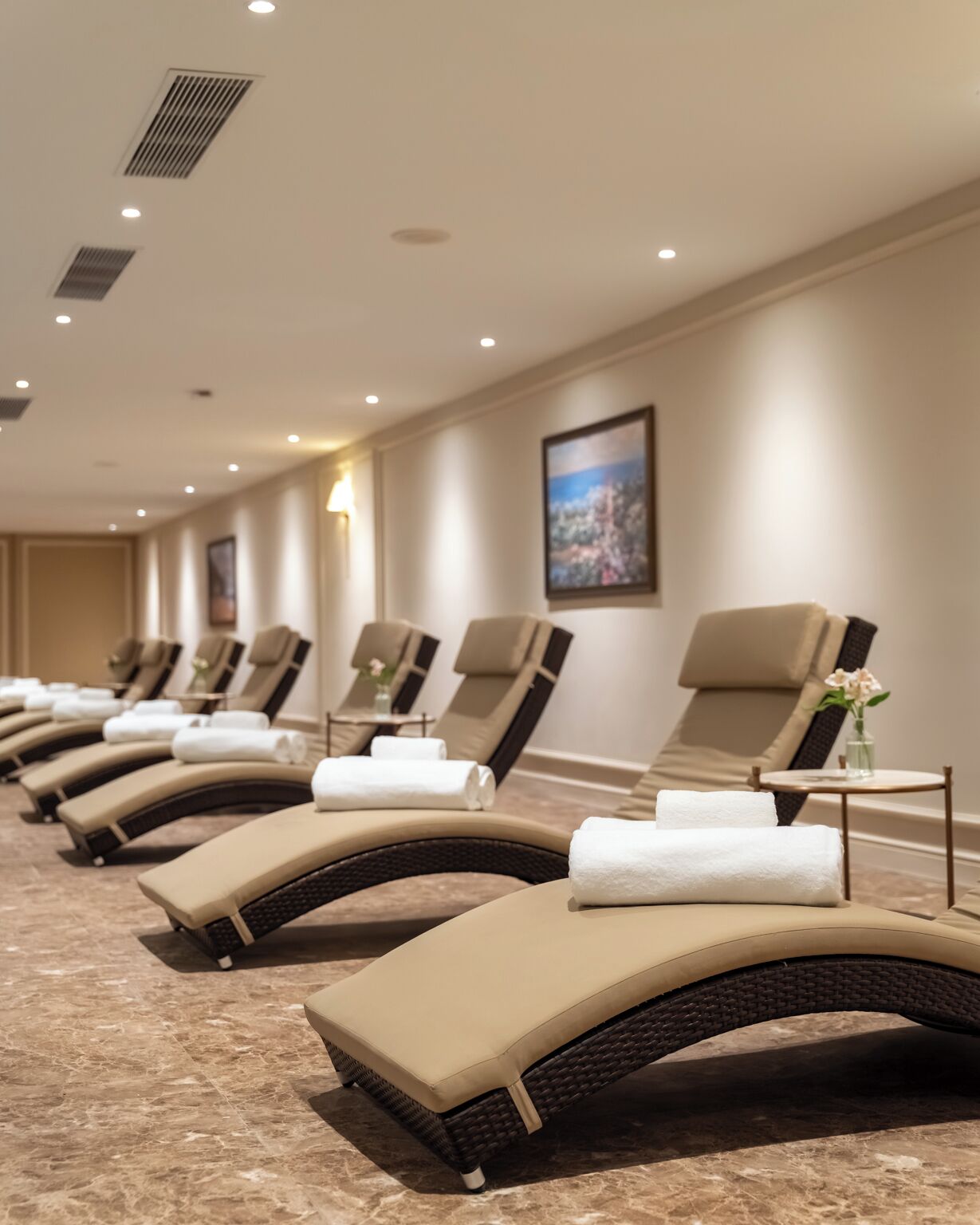A row of sun loungers with towels, arranged in a hotel lobby with a marble floor and a framed picture on the wall.