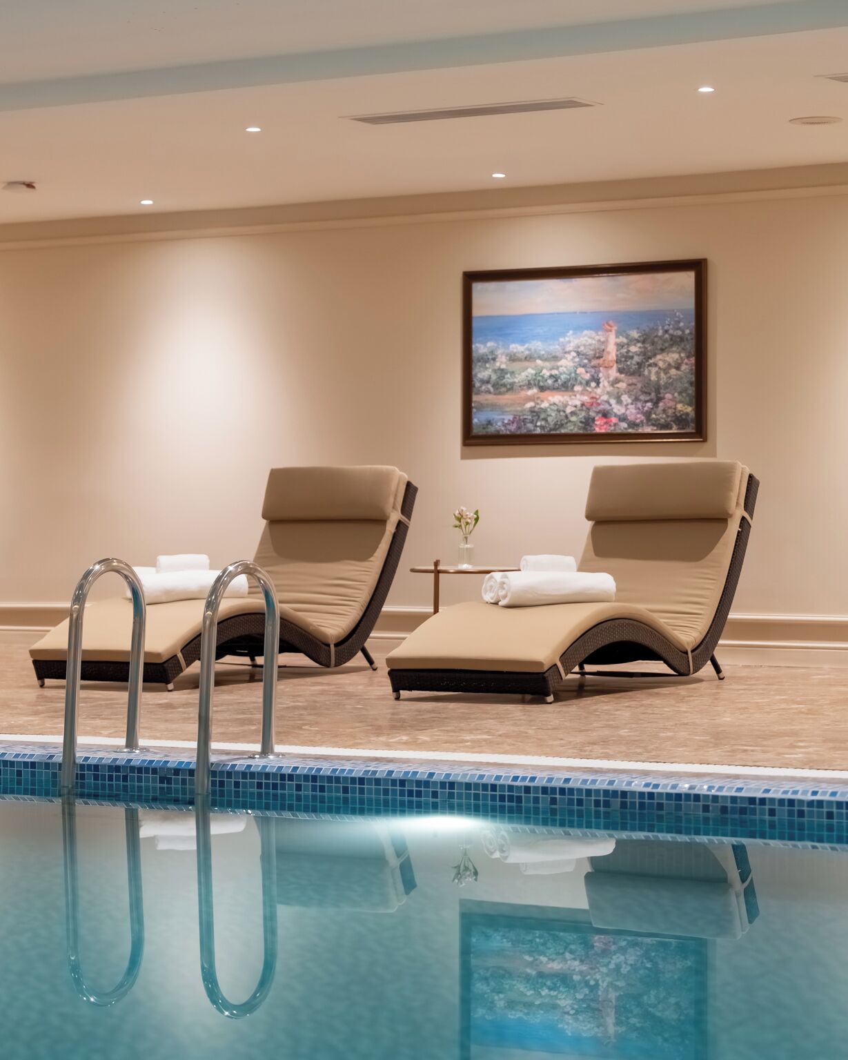 A poolside area with two lounge chairs and a small table with a vase.