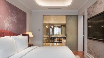 A modern hotel room with a large bed, a glass-enclosed bathroom, and a flat-screen TV.
