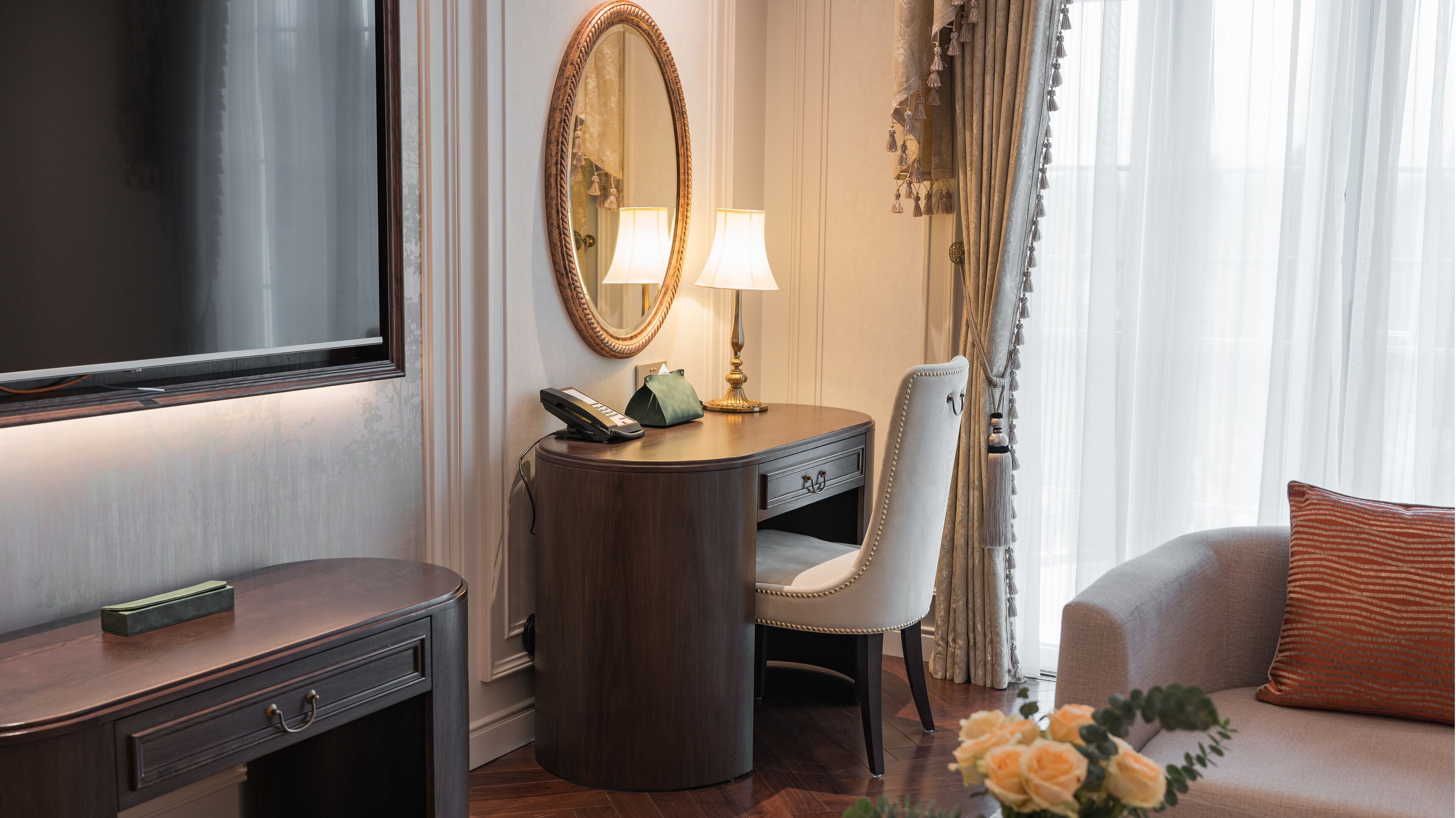 Une chambre d’hôtel équipée d’un grand téléviseur à écran plat, d’un bureau avec un téléphone, d’une chaise, d’un canapé et d’un miroir.