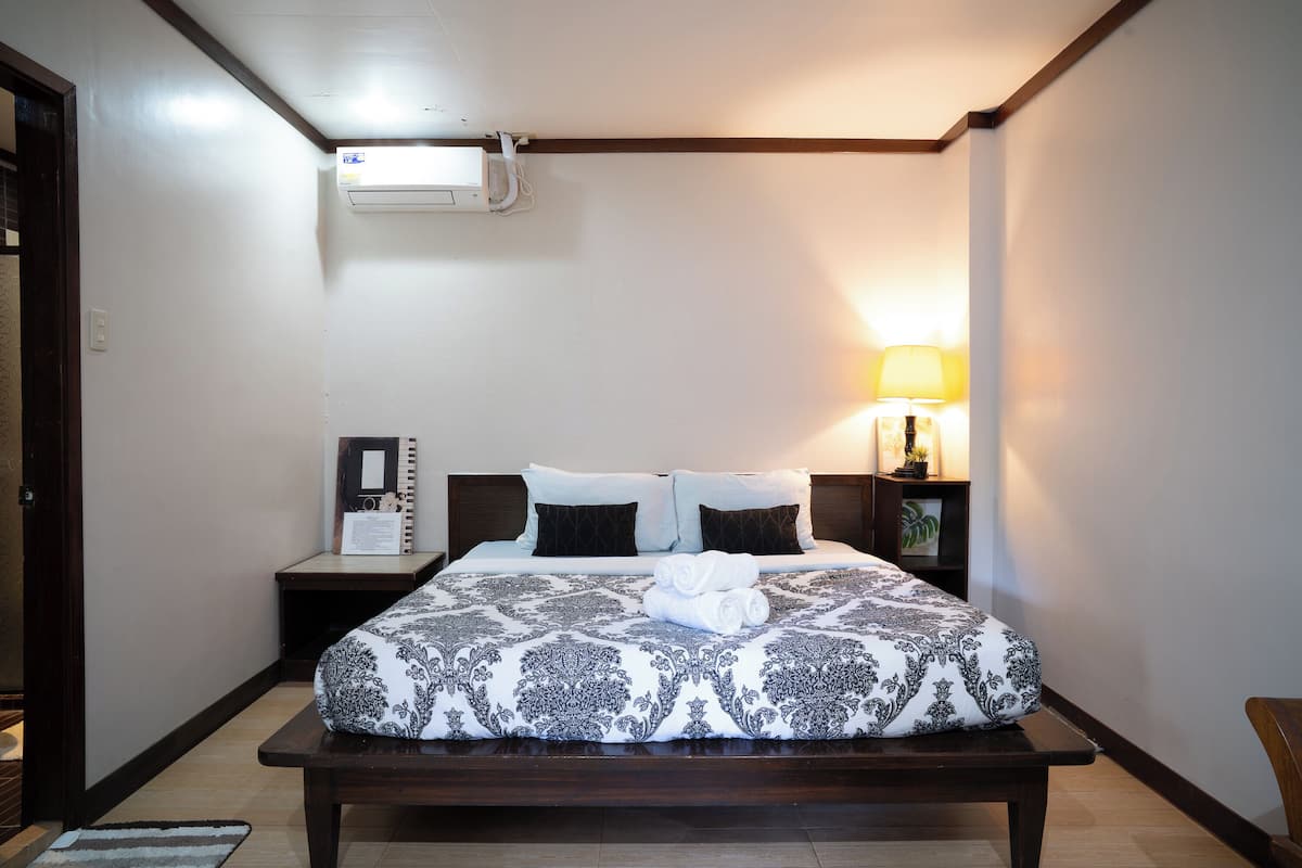 A neatly made bed with patterned bedding, a bedside lamp, and a small table with a lamp.