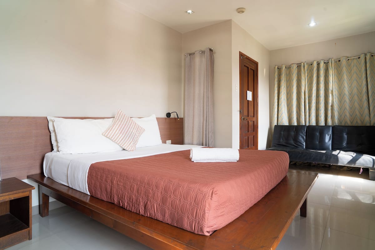 A hotel room with a large bed, a wooden bench, a sofa, and a door leading to a bathroom.