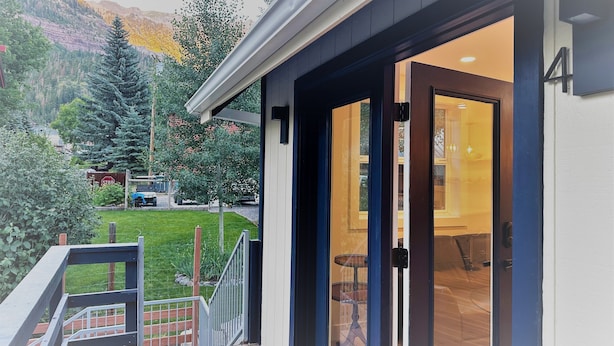 A modern house with a deck, a glass door leading to a room, and a mountain view in the background. - Outlaw Inn Unit 4.  Newly Remodeled large unit! 2 minutes walk to Main Street.  (Ouray)