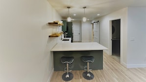 A modern kitchen with a central island, wooden shelves, and two bar stools. - Outlaw Inn Unit 4.  Newly Remodeled large unit! 2 minutes walk to Main Street.  (Ouray)