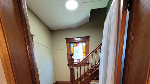 Un escalier en bois avec une rampe, une petite chaise et un tapis posé sur un plancher en bois.