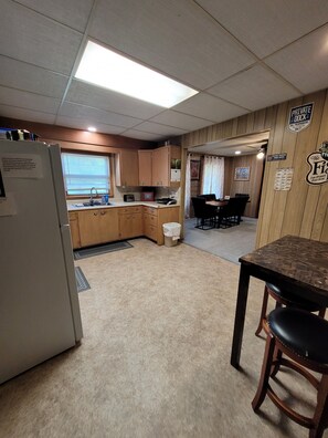 A compact kitchen with wooden cabinets, a refrigerator, a sink, and a dining area with a table and chairs. - Main Street Home-Locally Owned-No Cleaning Fees-Pets Allowed (Webster)