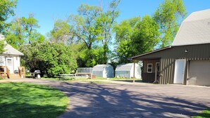 Une allée pavée mène à un bâtiment doté d’un garage, d’un espace de pique-nique couvert et d’une zone clôturée avec de l’herbe verte.