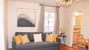 Een woonkamer met een grijze bank, een vloerkleed, een kroonluchter en een schilderij aan de muur.