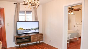 Een woonkamer met een flatscreen televisie op een houten standaard, een kroonluchter en een houten vloer.