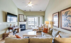 Cozy living room with a fireplace, comfortable seating, and a ceiling fan. Enjoy the view from the large window.