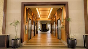 Un couloir d’hôtel avec un sol carrelé, des portes en bois et des plantes en pot.