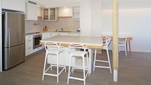 A modern kitchen with white cabinetry, a stainless steel refrigerator, a wooden island with bar stools, and a cat tree. - Portsea North Apt 5  (Mooloolaba)