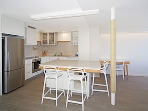 Eine moderne Küche mit weißen Schränken, einem Edelstahl-Kühlschrank, einer Holz-Kochinsel mit Barhocker und einer Katzenliege.