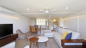 A spacious living room with a flat-screen TV, a sofa, a coffee table, and a dining area with chairs and a table. - Portsea North Apt 5  (Mooloolaba)