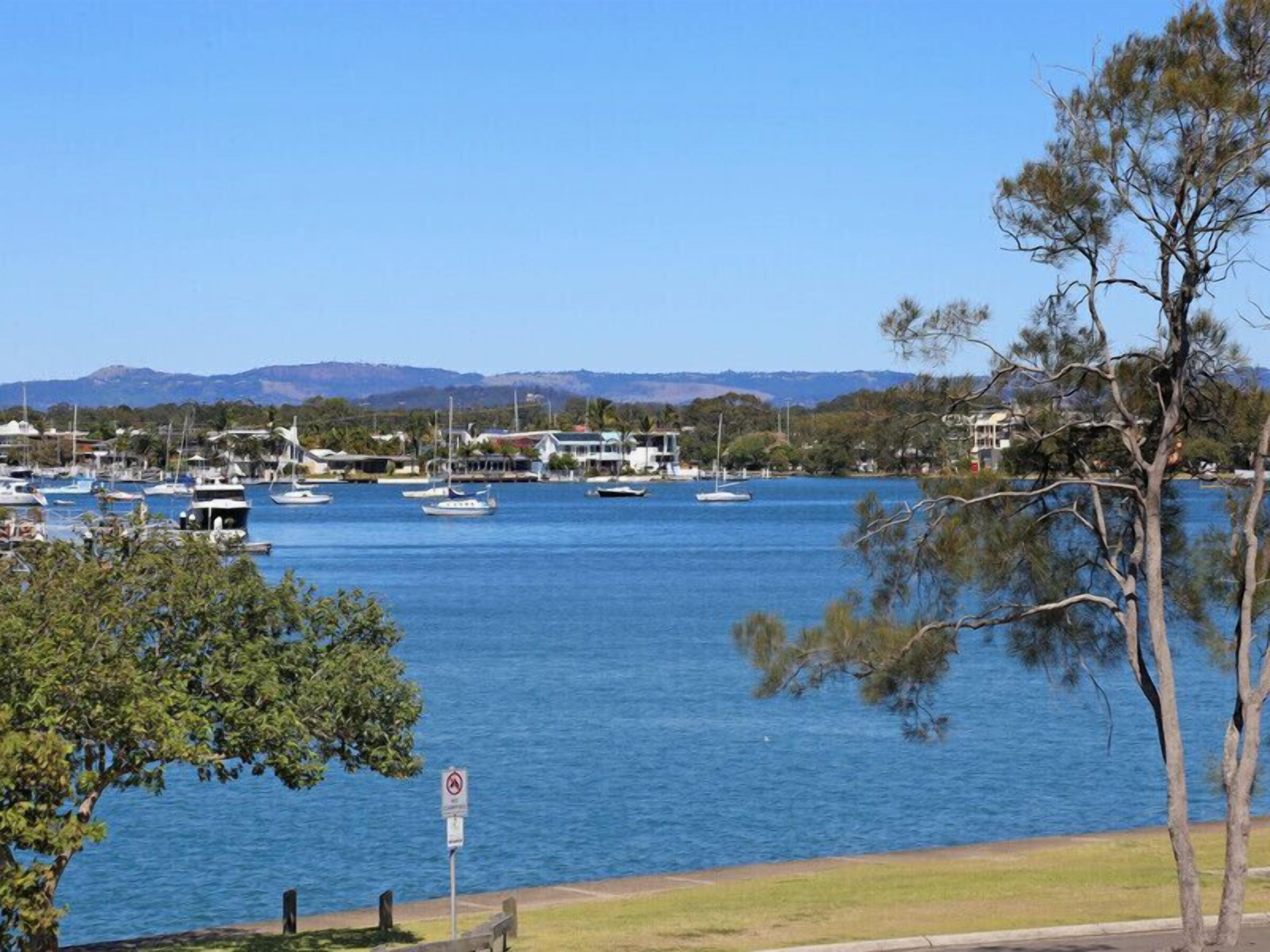 A marina with boats docked, a clear blue sky, and a mountainous landscape in the background.