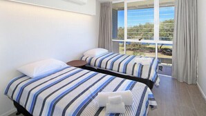A hotel room with two beds, a large window with curtains, and an air conditioning unit on the wall. - Portsea North Apt 5  (Mooloolaba)