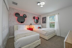 Une chambre avec deux lits, une décoration murale à l’effigie de Mickey Mouse, une table de chevet et une fenêtre avec des rideaux.