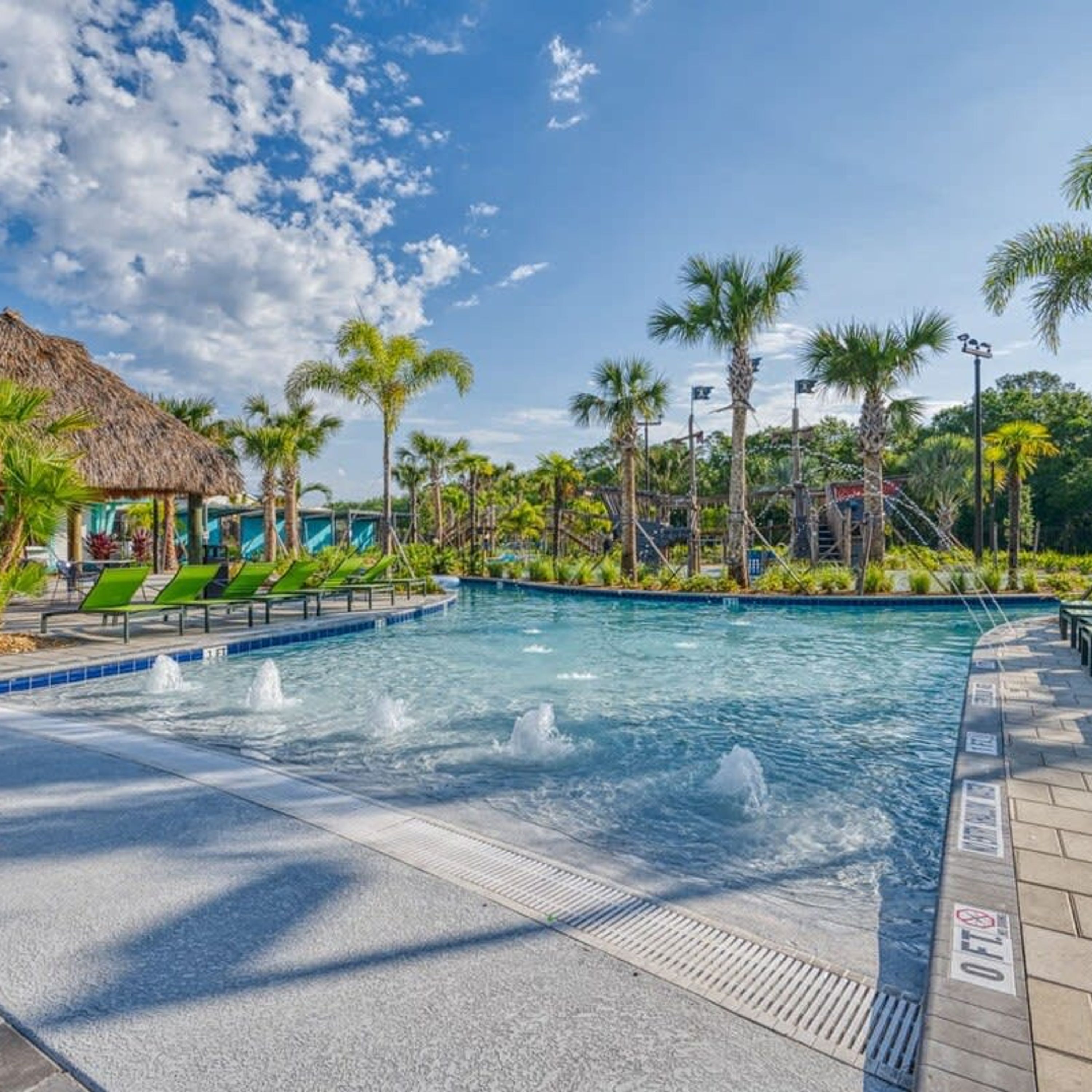 A swimming pool with a thatched-roof structure, palm trees, and a clear blue sky.