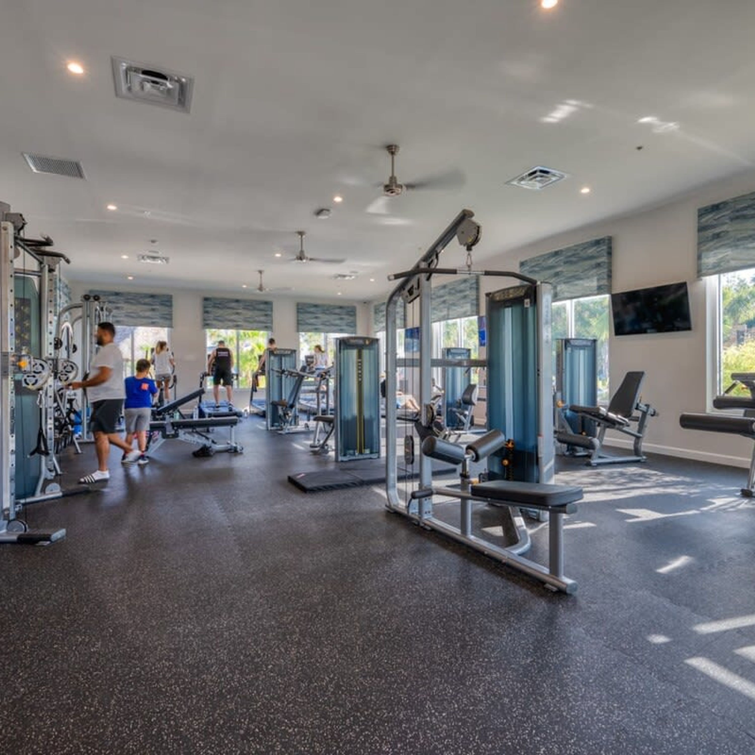 Une salle de sport équipée de divers appareils d’exercice, dotée de grandes fenêtres et d’un ventilateur de plafond.