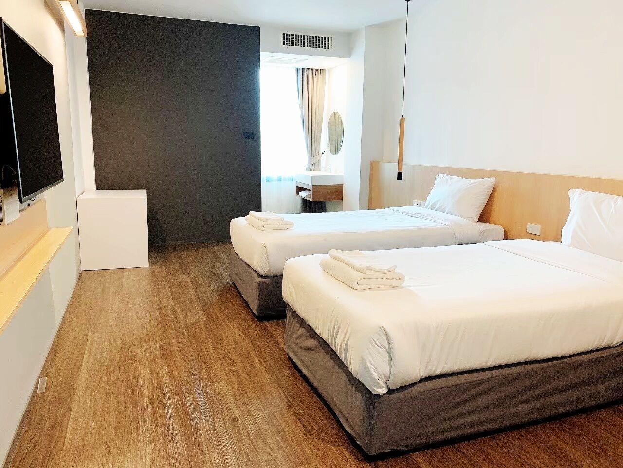 Ein Hotelzimmer mit zwei Betten, einem Fernseher, einem kleinen Tisch und einem Fenster mit Vorhängen.