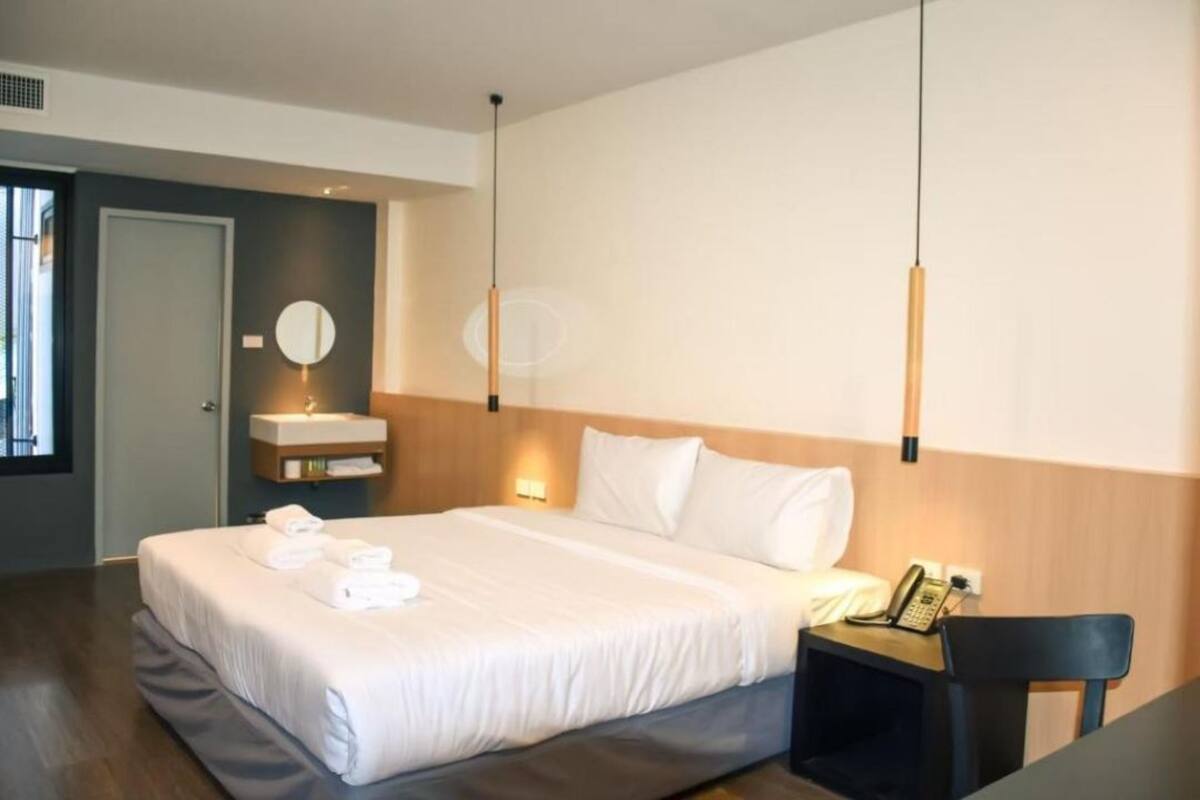 A modern hotel room with a large bed, bedside table with a phone, and a wall-mounted mirror.