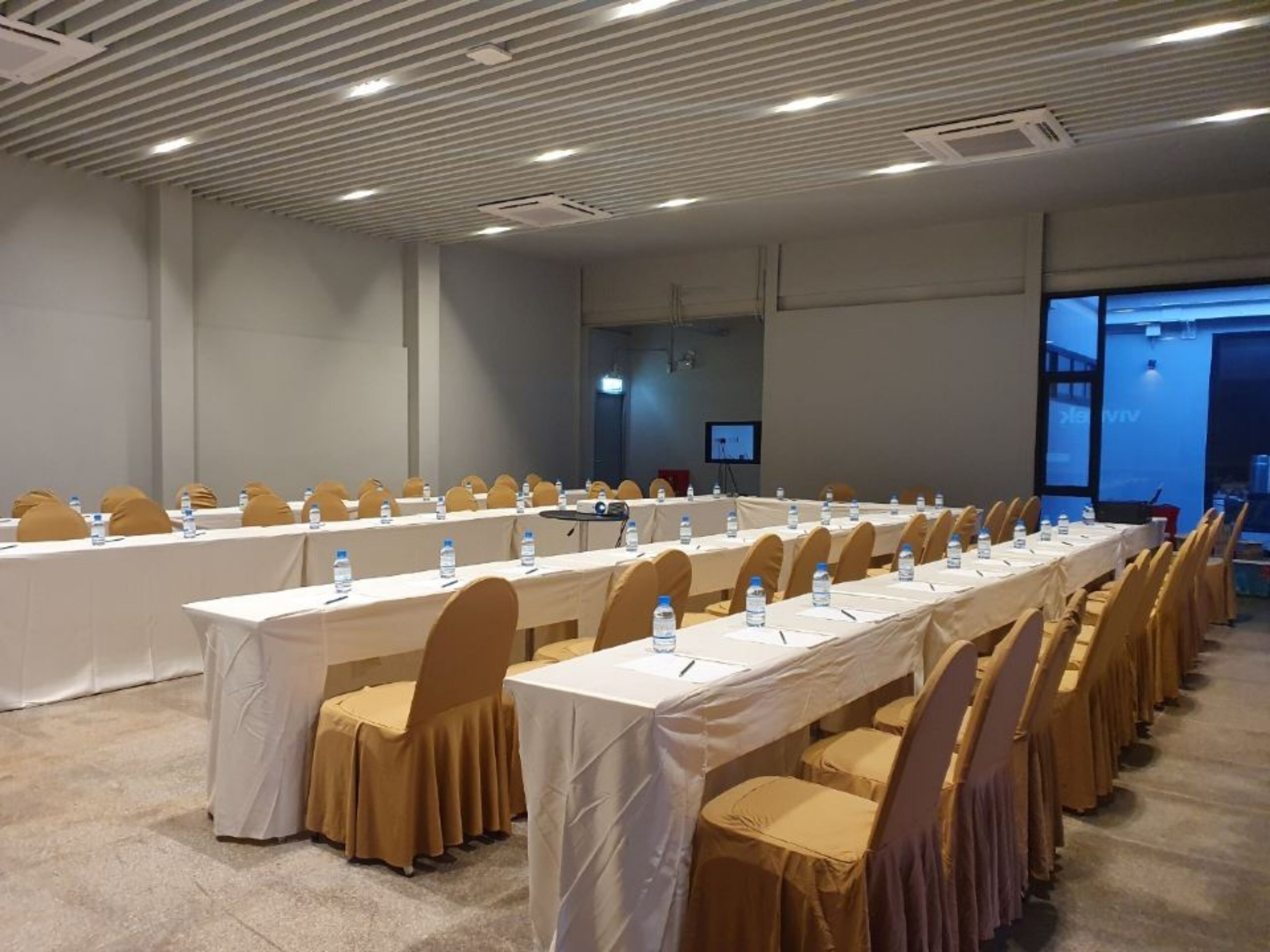 Un salón de conferencias con mesas largas, sillas y botellas de agua.