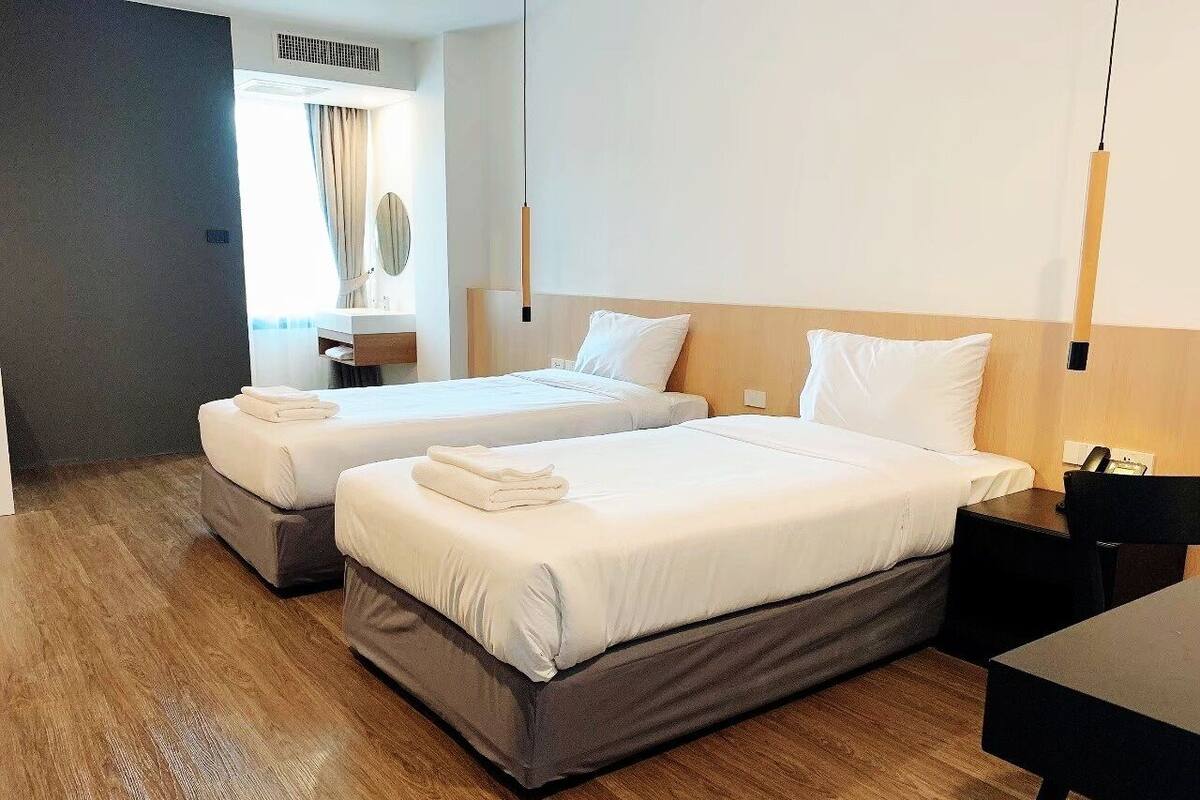 A hotel room with two beds, a wooden floor, a desk, and a mirror.