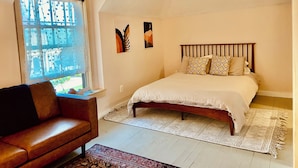 Ein Schlafzimmer mit einem Bett, einem Holz-Kopfteil, einem Fenster mit Vorhängen, einem braunen Ledersofa und einem gemusterten Teppich.