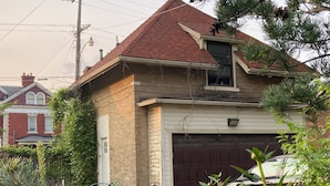 Ein zweigeschossiges Haus mit rotem Ziegeldach, einer Garage und einem Vorgarten mit grünen Pflanzen und Metallstühlen.