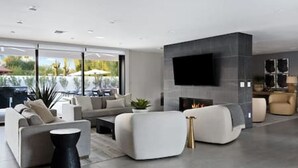 Un salon moderne doté d’un grand téléviseur à écran plat fixé sur un mur sombre, d’une cheminée et d’un espace détente avec des canapés et une table basse.