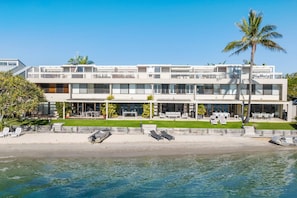 A modern two-story building with a balcony, outdoor seating, and a view of the water.