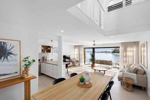 A modern interior with a dining area, kitchen, and living space with a view of the water.