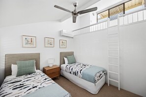 A bedroom with two beds, a ceiling fan, a ladder, and framed pictures on the wall.