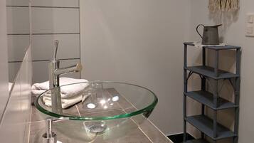 Une salle de bain moderne avec un lavabo en verre, un porte-serviettes, une étagère et un support à papier toilette.