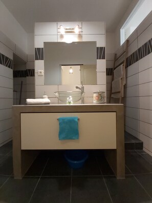 Une salle de bain moderne avec un lavabo en verre, un miroir au-dessus du lavabo et un porte-serviettes fixé au mur.