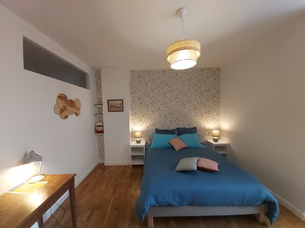 Une chambre à coucher comprenant un lit, des lampes de chevet, une table de nuit en bois, un bureau avec une lampe et une étagère fixée au mur.