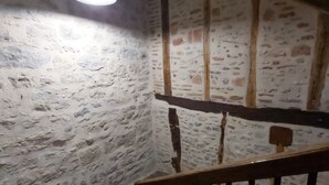 A staircase with a wooden railing, a stone wall, and a hanging light fixture.