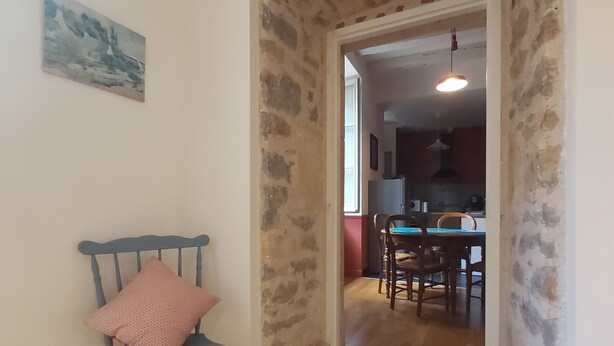 A room with a stone archway leading to a dining area. A blue chair with a patterned cushion is positioned near the archway.