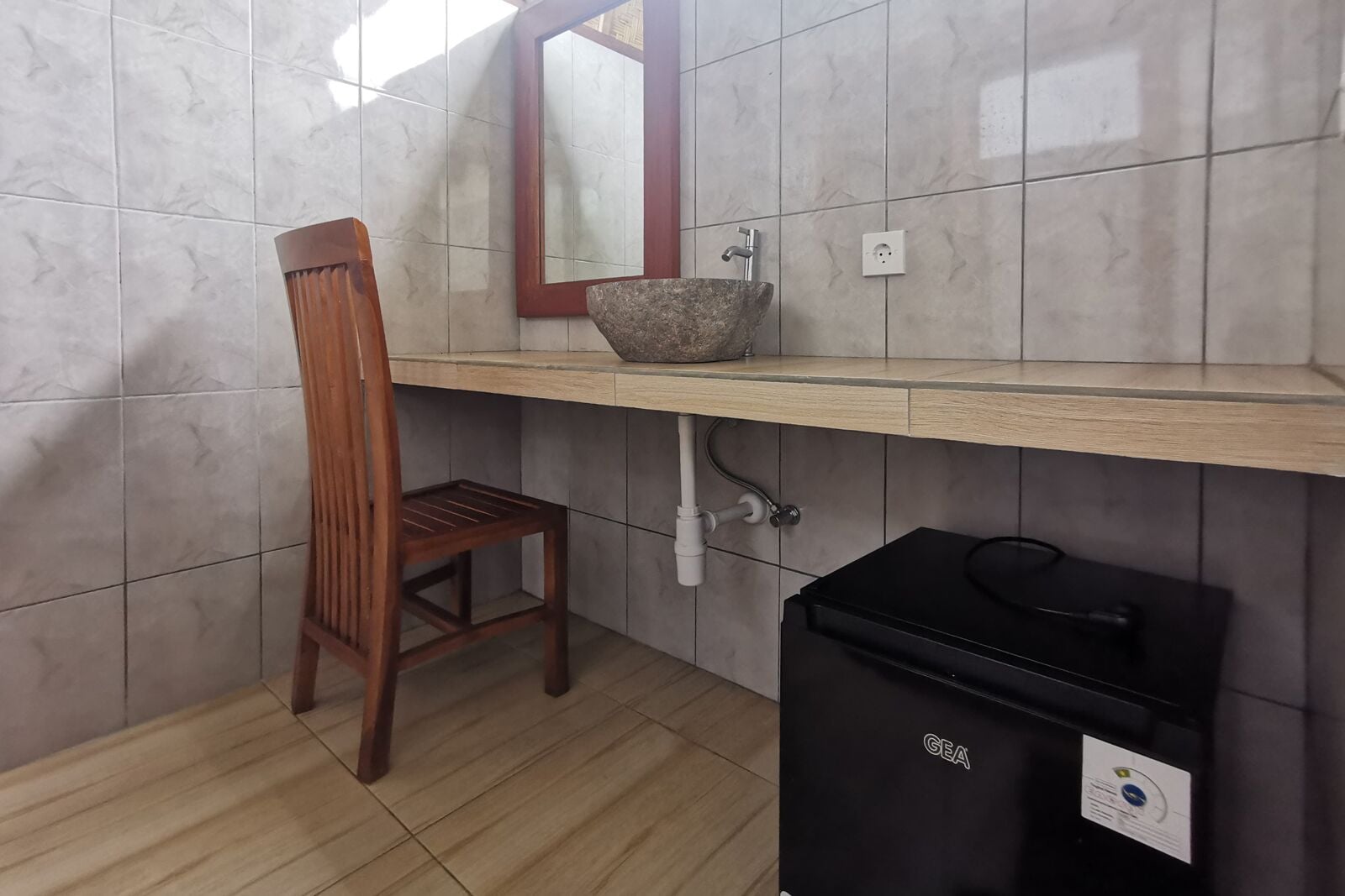 A bathroom with a wooden chair, a sink with a stone basin, and a GEA trash bin.