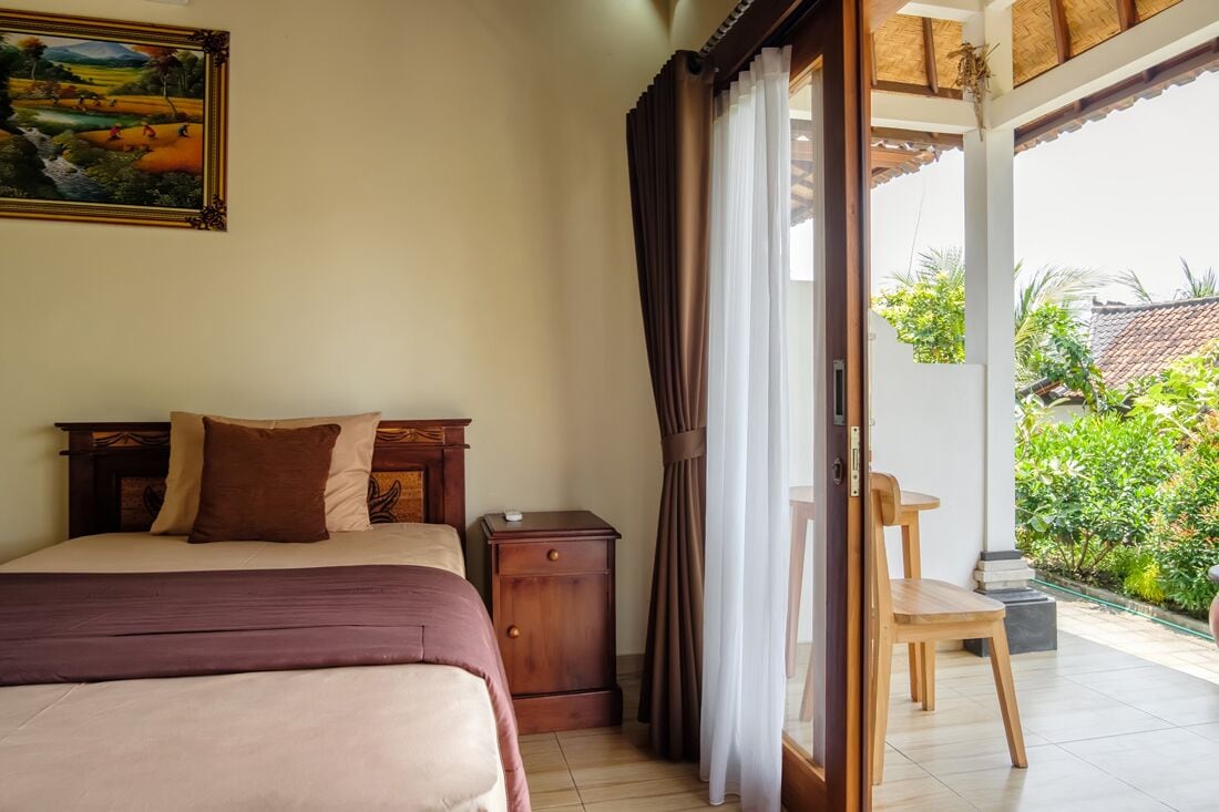 Un dormitorio con cama, mesita de noche, una silla y vistas a un jardín a través de una ventana.