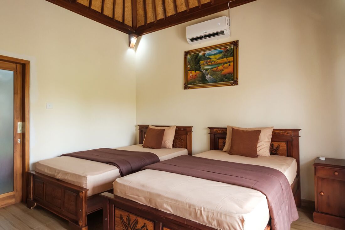 A room with two beds, wooden headboards, a painting on the wall, and an air conditioning unit.