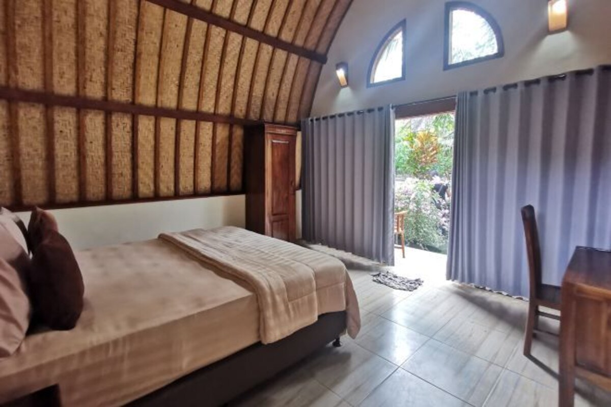 Ein Schlafzimmer mit einem großen Bett, einer Holzbalkendecke und Blick durch ein Fenster.