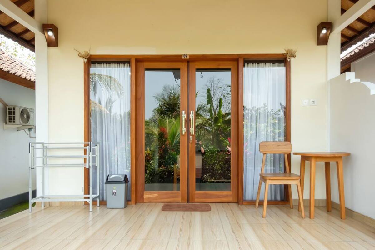 A room with a sliding glass door leading to a garden, a small table and chair, and a metal drying rack.