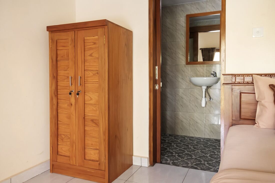 A room with a wooden wardrobe, a bathroom with a sink and mirror, and a bed with a headboard.