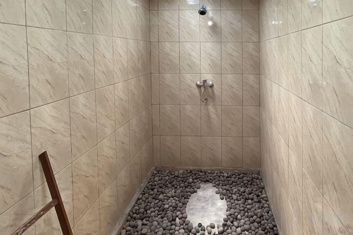 A tiled shower area with a pebble floor and a wooden chair.