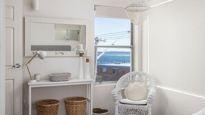 A white bathroom with a large mirror, a white chair, wicker baskets, and a view of the sea through a window. - Bayview Towers 10 With Harbour Views (Nelson Bay)